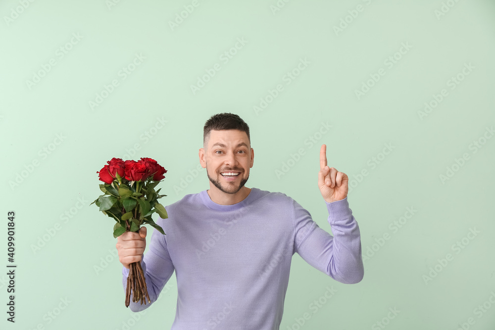 Handsome man with bouquet of beautiful flowers pointing at something on color background Handsome man with bouquet of beautiful flowers pointing at something on color background