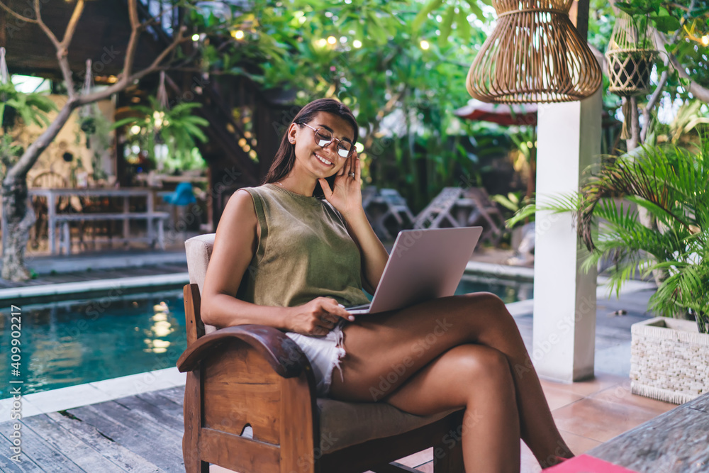 Joyful ethnic woman browsing laptop on terrace