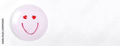 Cute smiley face made of decorative hearts and red ribbon on the plate. Setting the table to celebrate Valentine's Day. Wide banner with copy space