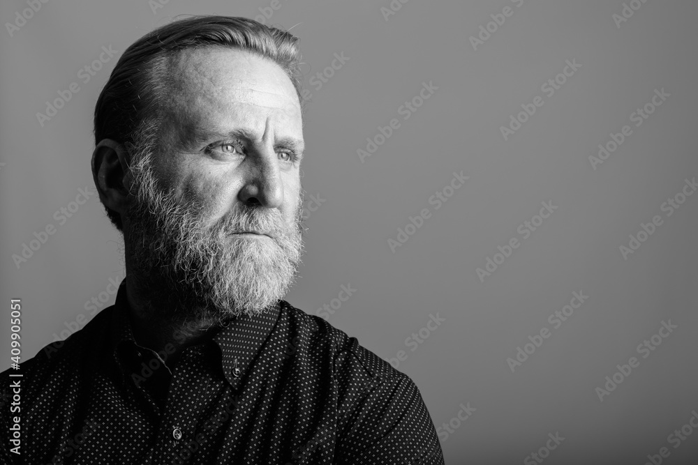 Fototapeta premium Studio shot of mature bearded man thinking while looking away in gray background