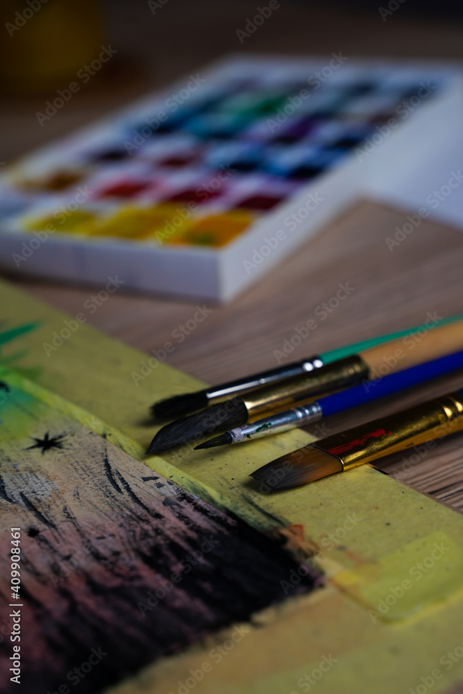 Watercolor paints and brushes on a wooden table. Paints background.