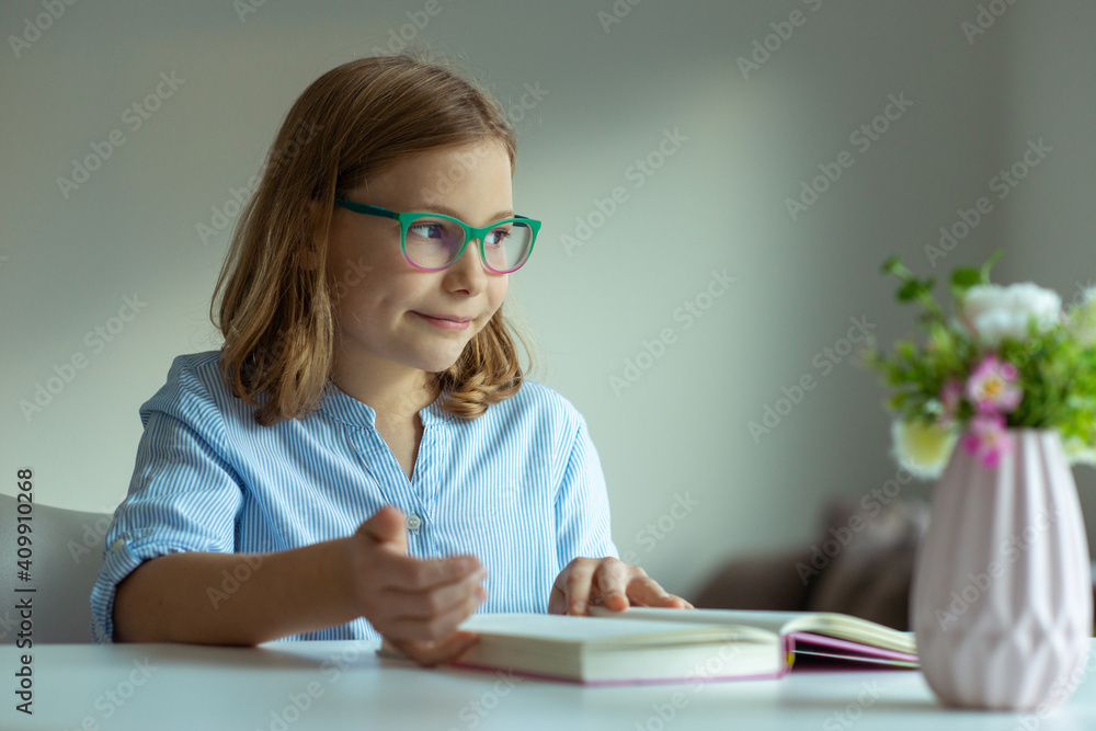 Pretty teen girl reading book at desk during pandemic distance learning Pretty teen girl reading book at desk during pandemic distance learning
