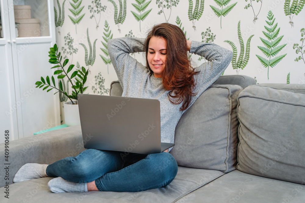 Smiling young female freelancer sitting on couch enjoying working remotely from home. Happy woman student studying on online courses indoors Smiling young female freelancer sitting on couch enjoying working remotely from home. Happy woman student studying on online courses indoors