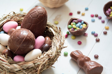 Chocolate eggs and easter almonds on bird nest, chocolate bunny and sweets on white wooden table