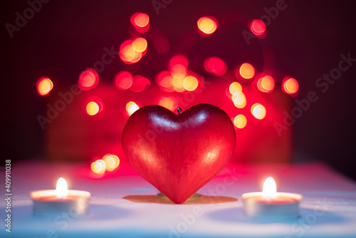 Red love heart illuminated by two candles with red and yellow light bubbles in the background