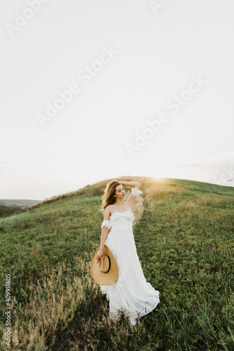 Young beautiful woman in boho style dress and hat on nature at sunset.