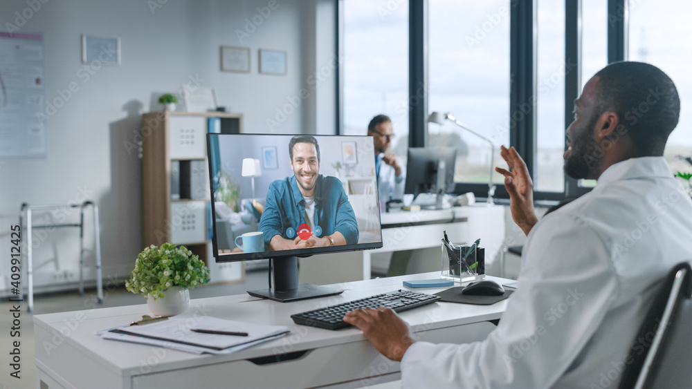African American Medical Doctor is Making a Video Call with Patient on a Computer with Green Screen Display in a Health Clinic. Assistant in Lab Coat is Talking About Health Issues in Hospital Office. African American Medical Doctor is Making a Video Call with Patient on a Computer with Green Screen Display in a Health Clinic. Assistant in Lab Coat is Talking About Health Issues in Hospital Office.
