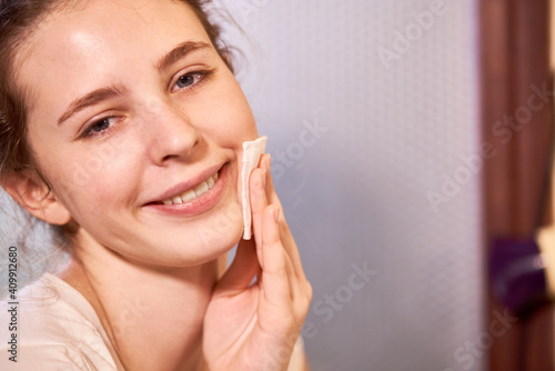 Portrait of young beautiful teenage girl wiping clean face with matifying toner or micellar water