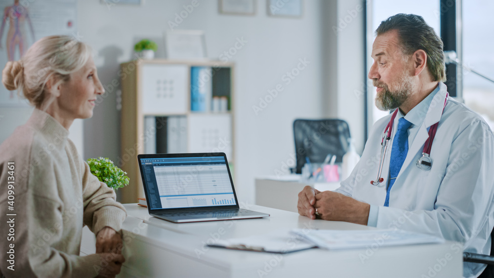 Friendly Family Medical Doctor is Explaining Diagnosis to a Senior Patient and Showing Medical Test Results on a Laptop Computer in a Health Clinic. Bright Modern Hospital Office. Friendly Family Medical Doctor is Explaining Diagnosis to a Senior Patient and Showing Medical Test Results on a Laptop Computer in a Health Clinic. Bright Modern Hospital Office.