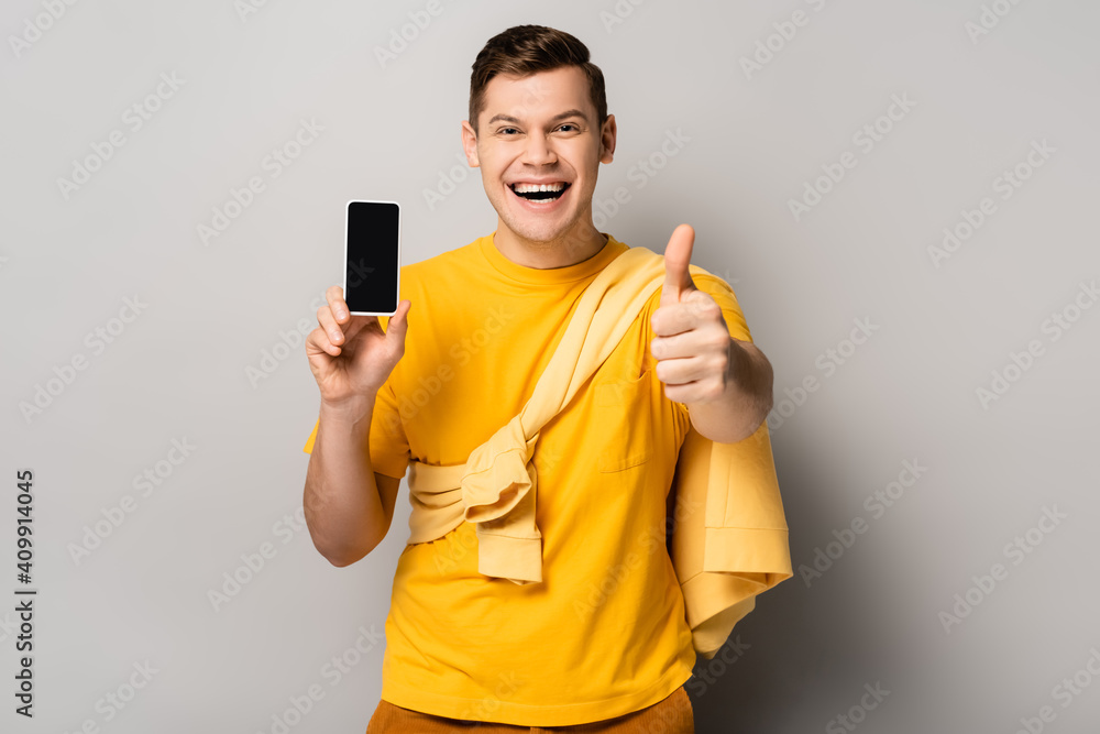 Cheerful man showing like and holding cellphone with blank screen on grey background Cheerful man showing like and holding cellphone with blank screen on grey background