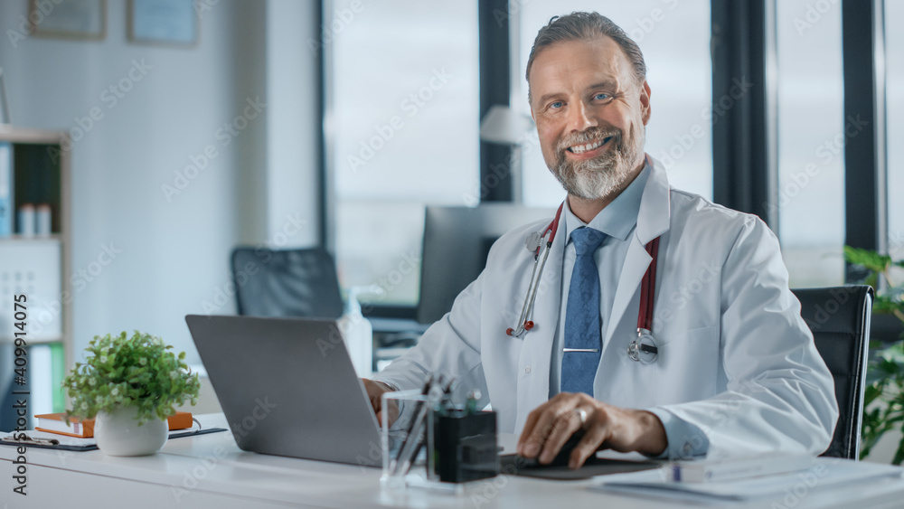 Middle Aged Family Medical Doctor with a Beard is Working in a Health Clinic. Successful Senior Physician in White Lab Coat Looks at the Camera and Smiles in Hospital Office. 