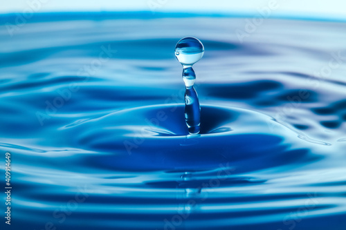 Dark blue water droplets splash close up on the water surface. It creates a water wave and a perfect crown