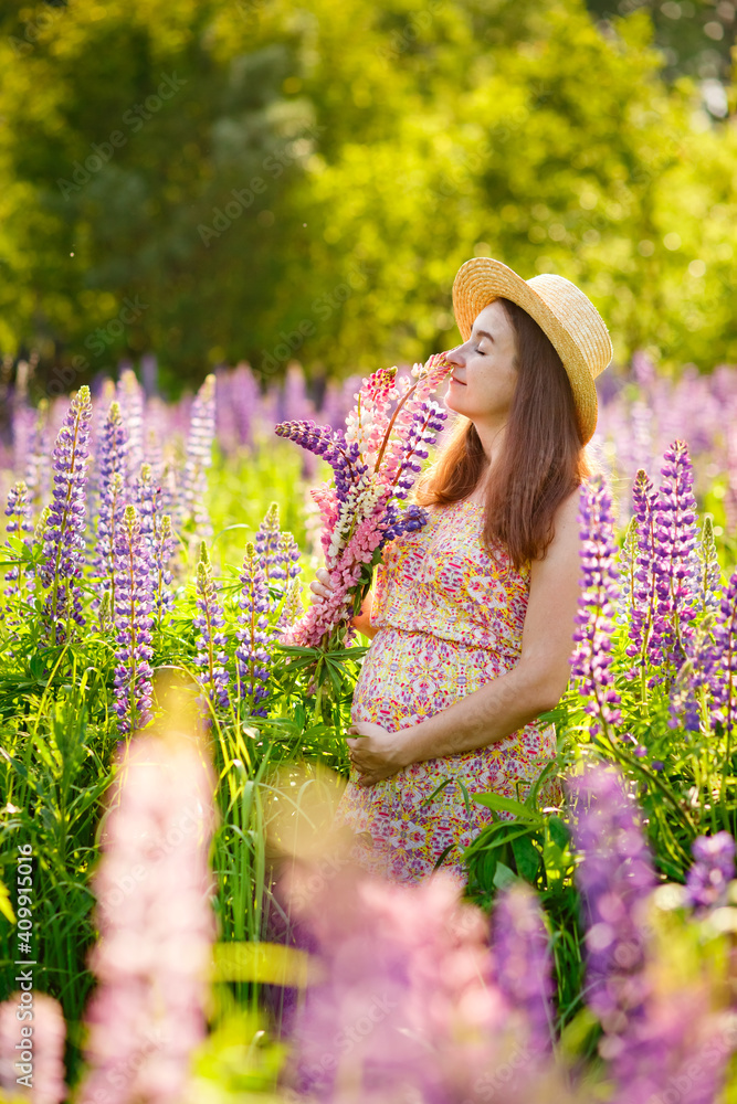 A pregnant woman in a summer dress with a flower crown with a large luxurious blue lupin sits in a field of blooming lupin A pregnant woman in a summer dress with a flower crown with a large luxurious blue lupin sits in a field of blooming lupin