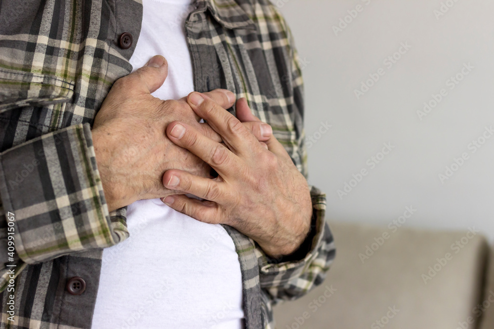 Photo of a senior male with chest pain. Elderly man suffering from heartburn or chest discomfort symptoms. Men having a pain in the heart area. Old man with eyeglasses having heart attack at home.