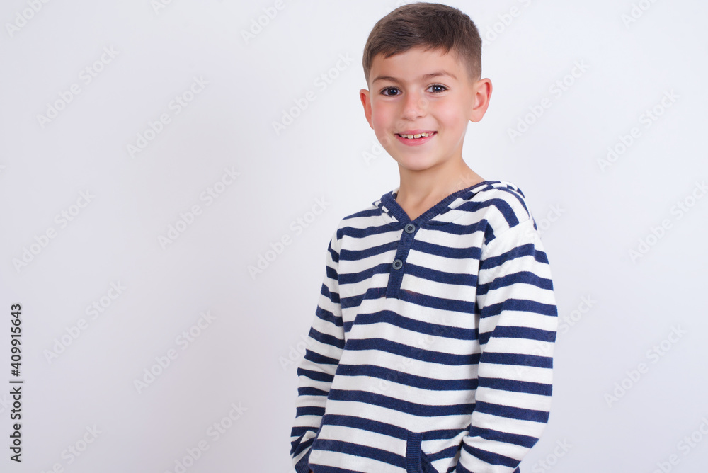 Portrait of successful little cute boy kid wearing stripped t-shirt against white wall, smiling broadly with self-assured expression. Confidence and business concept. Portrait of successful little cute boy kid wearing stripped t-shirt against white wall, smiling broadly with self-assured expression. Confidence and business concept.