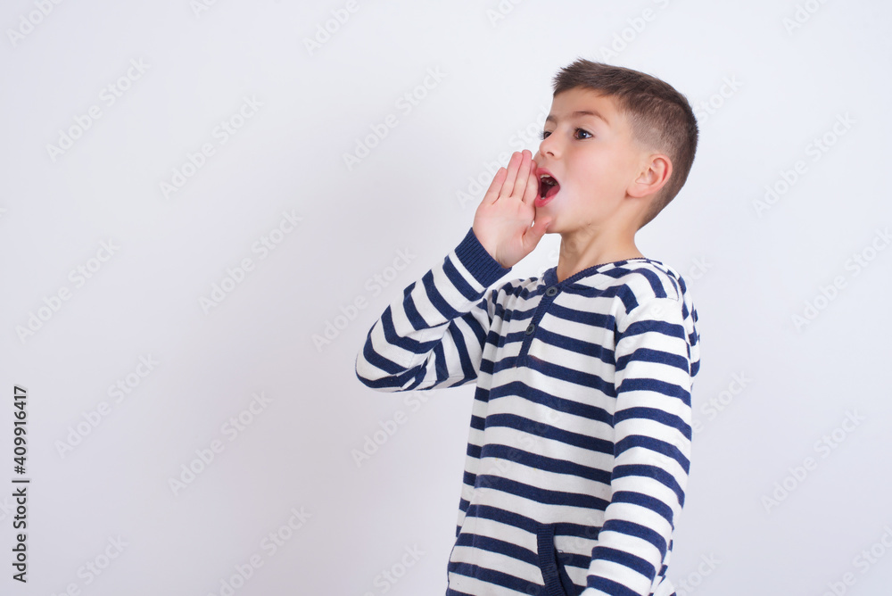 little cute boy kid wearing stripped t-shirt against white wall profile view, looking happy and excited, shouting and calling to copy space. little cute boy kid wearing stripped t-shirt against white wall profile view, looking happy and excited, shouting and calling to copy space.