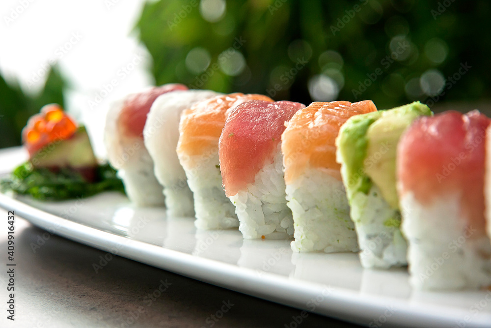 Assortment of Japanese sushi rolls nigiri, sashimi, maki, salmon, tuna and avocado served in long rectangular plate over stone background, close up view Assortment of Japanese sushi rolls nigiri, sashimi, maki, salmon, tuna and avocado served in long rectangular plate over stone background, close up view