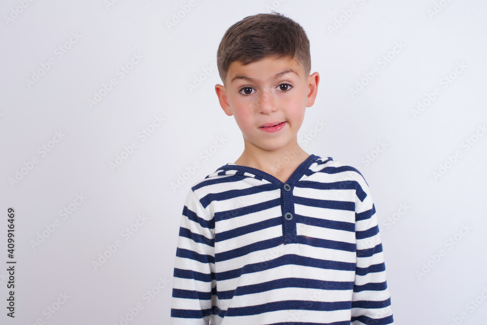 little cute boy kid wearing stripped t-shirt against white wall being nervous and scared biting lips looking camera with impatient expression, pensive. little cute boy kid wearing stripped t-shirt against white wall being nervous and scared biting lips looking camera with impatient expression, pensive.