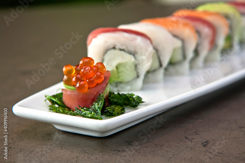 Assortment of Japanese sushi rolls nigiri, sashimi, maki, salmon, tuna and avocado served in long rectangular plate over stone background