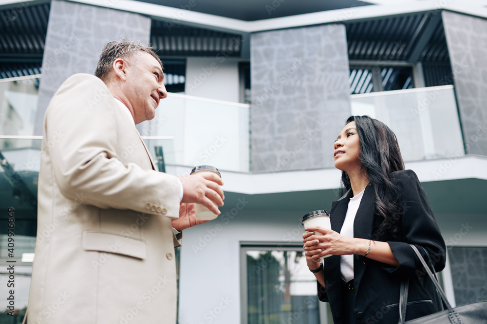 Pretty young Asian businesswoman talking to senior colleague when they are drinking take out coffee outdoors Pretty young Asian businesswoman talking to senior colleague when they are drinking take out coffee outdoors