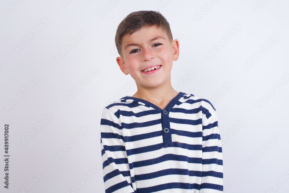 Portrait of mysterious little cute boy kid wearing red stripped t-shirt against white wall looking up with enigmatic smile. Advertisement concept. Portrait of mysterious little cute boy kid wearing red stripped t-shirt against white wall looking up with enigmatic smile. Advertisement concept.
