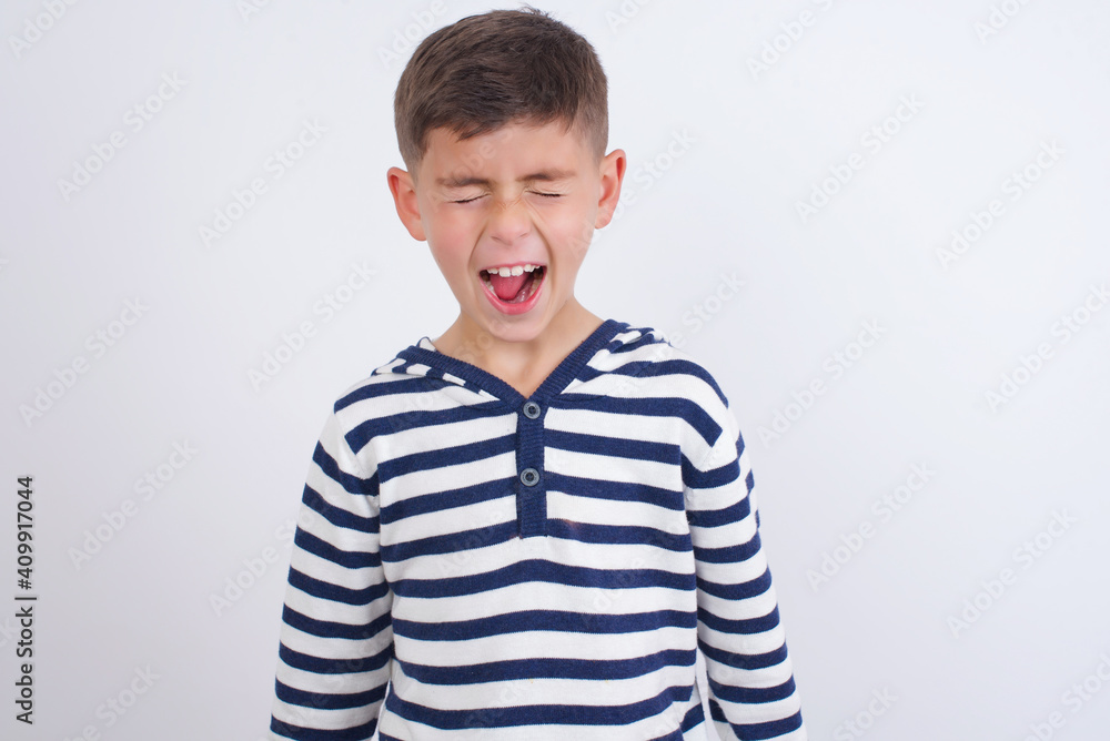 Stressful little cute boy kid wearing red stripped t-shirt against white wall screams in panic, closes eyes in terror, keeps hands on head, finds out terrified news, can't believe it. Stressful little cute boy kid wearing red stripped t-shirt against white wall screams in panic, closes eyes in terror, keeps hands on head, finds out terrified news, can't believe it.