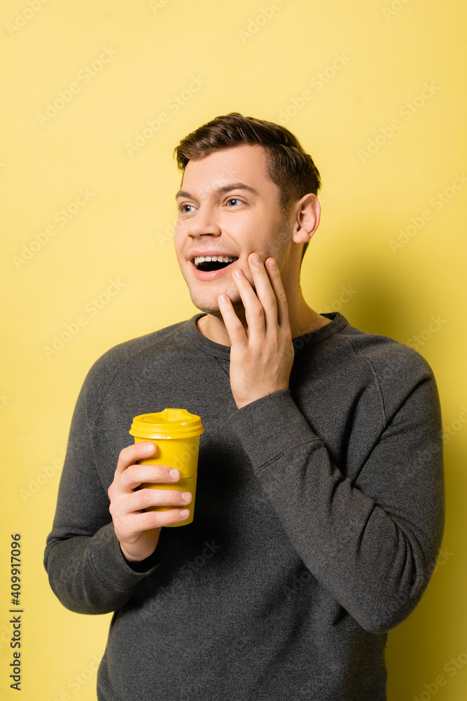 Fototapeta premium Positive man holding coffee to go on yellow background
