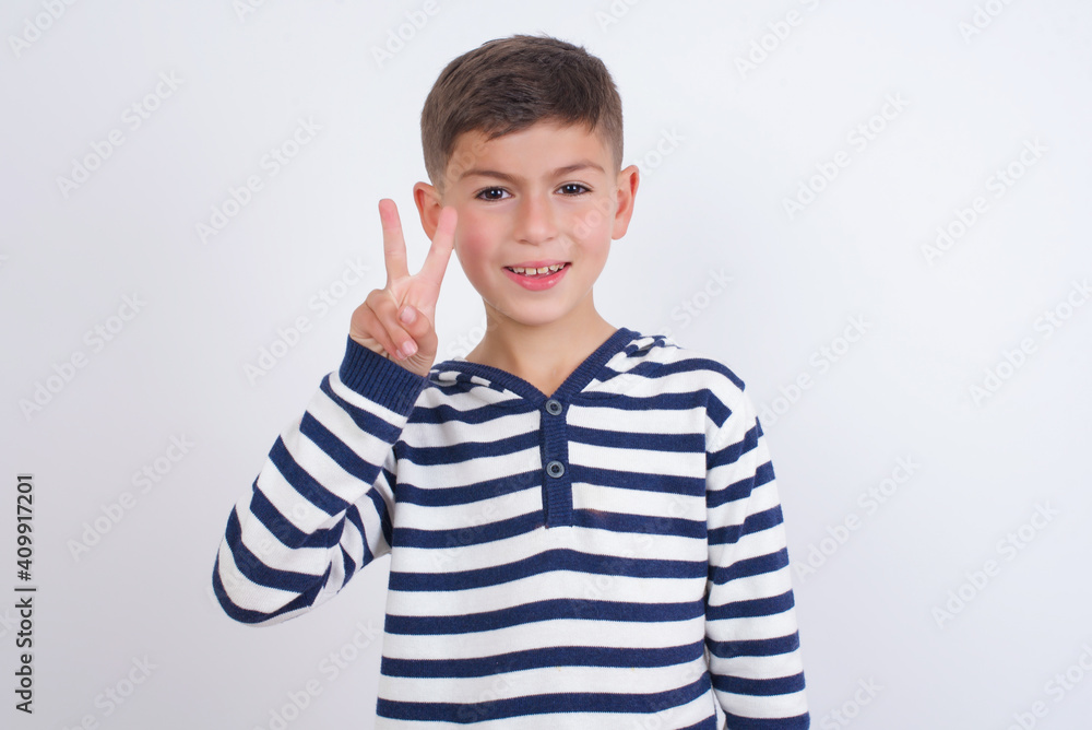 little cute boy kid wearing red stripped t-shirt against white wall showing and pointing up with fingers number two while smiling confident and happy. little cute boy kid wearing red stripped t-shirt against white wall showing and pointing up with fingers number two while smiling confident and happy.