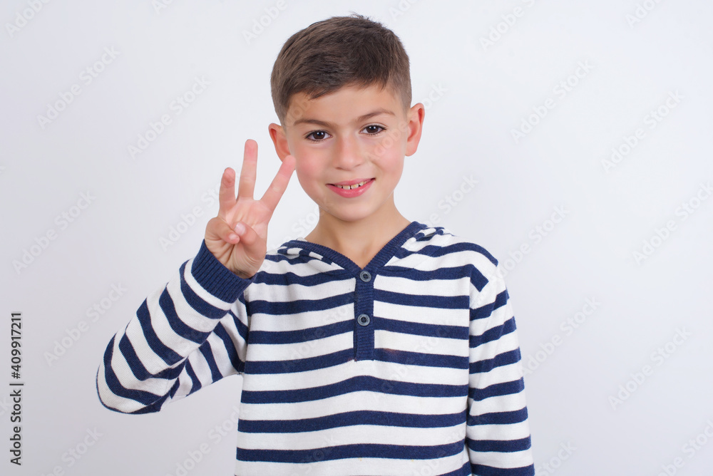 little cute boy kid wearing red stripped t-shirt against white wall showing and pointing up with fingers number three while smiling confident and happy. little cute boy kid wearing red stripped t-shirt against white wall showing and pointing up with fingers number three while smiling confident and happy.