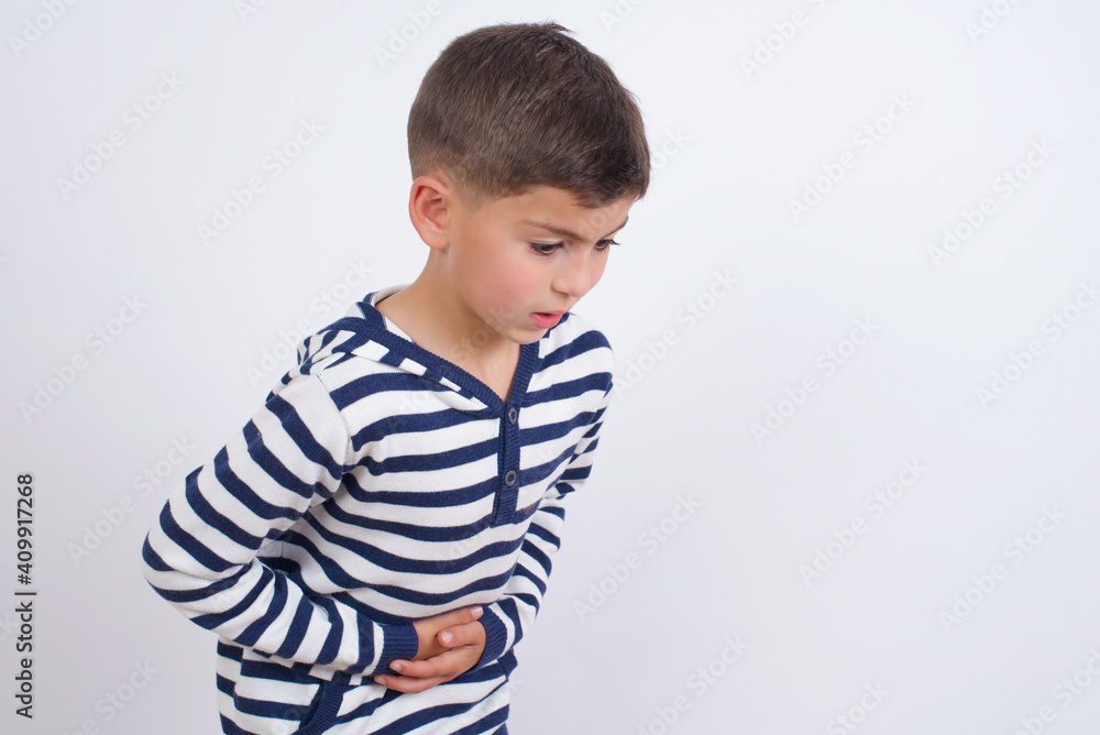 little cute boy kid wearing red stripped t-shirt against white wall suffering from strong stomachache. little cute boy kid wearing red stripped t-shirt against white wall suffering from strong stomachache.