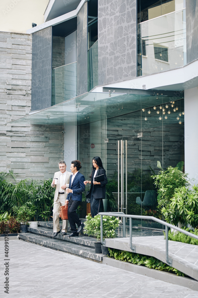 Group of business people walking out of office building with take out coffee in hands Group of business people walking out of office building with take out coffee in hands
