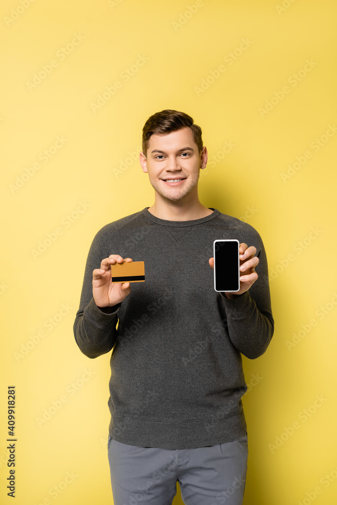 Smiling man showing credit card and smartphone on yellow background Smiling man showing credit card and smartphone on yellow background