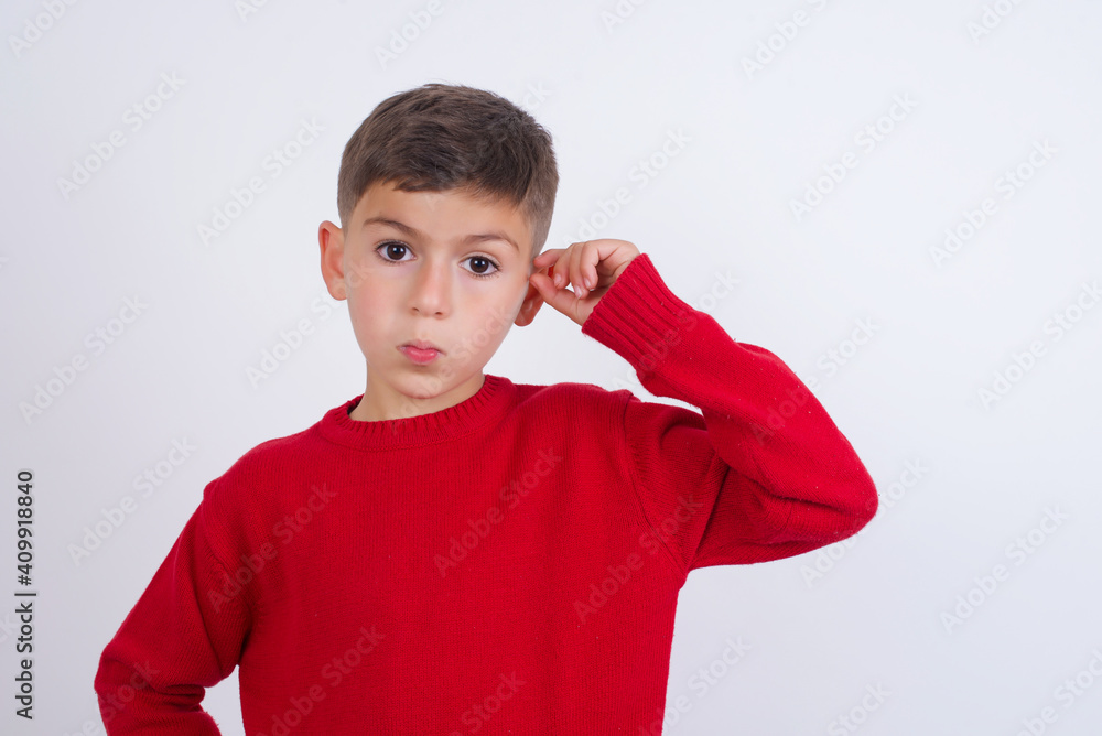 Upset Little cute boy kid wearing red knitted sweater against white wall shapes little gesture with hand demonstrates something very tiny small size. Not very much Upset Little cute boy kid wearing red knitted sweater against white wall shapes little gesture with hand demonstrates something very tiny small size. Not very much