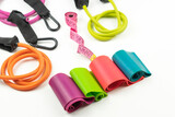 Colorful fitness elastic bands and expanders, a pink measuring tape lie on a white floor