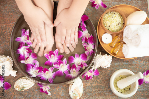 closeup view of woman soaking her hand and feet in dish with water and flowers on wooden floor. Spa treatment and product for female feet and hand spa. orchid flowers in ceramic bowl.