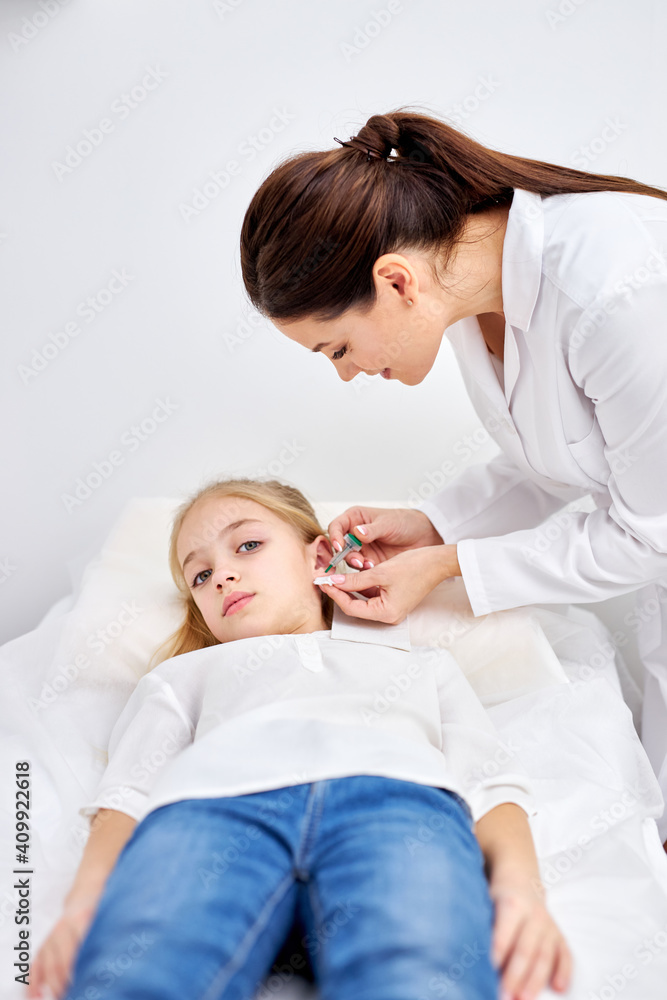 piercing ears to caucasian child girl in medical salon by a doctor in white robe using a special device. beauty and medicine concept piercing ears to caucasian child girl in medical salon by a doctor in white robe using a special device. beauty and medicine concept