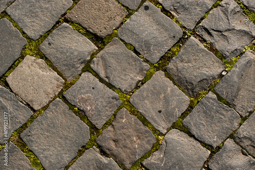 Abstract Background of Old Cobblestone Pavement Road with Green Moss. Grey pavement directly above