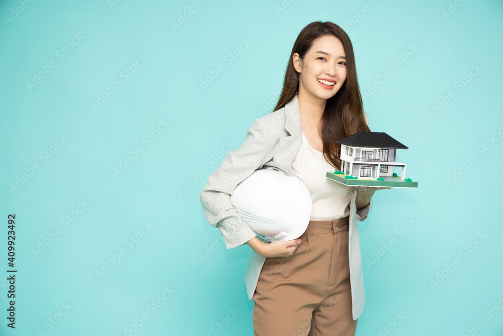 Home inspector Asian woman or engineer holding a white helmet and single-family home or detached house model isolated on green background Home inspector Asian woman or engineer holding a white helmet and single-family home or detached house model isolated on green background