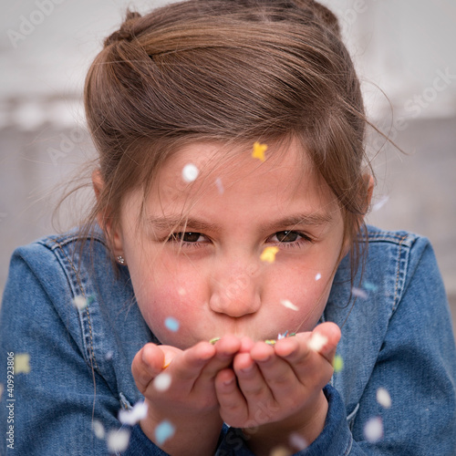 Young girl blowing a handful of confetti.