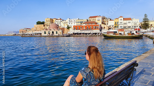 A young woman sits on a bench at The Old Venetian Harbor of Chania, Crete © abrada