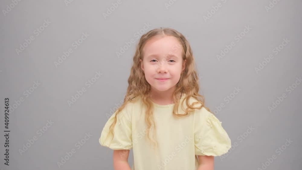 Little girl looks at the camera and laughs. Portrait of a child in the studio on a gray background close-up. Super slow motion. Little girl looks at the camera and laughs. Portrait of a child in the studio on a gray background close-up. Super slow motion.