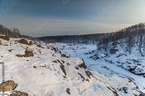 Winter landscape with frozen river, snow, rocks and trees