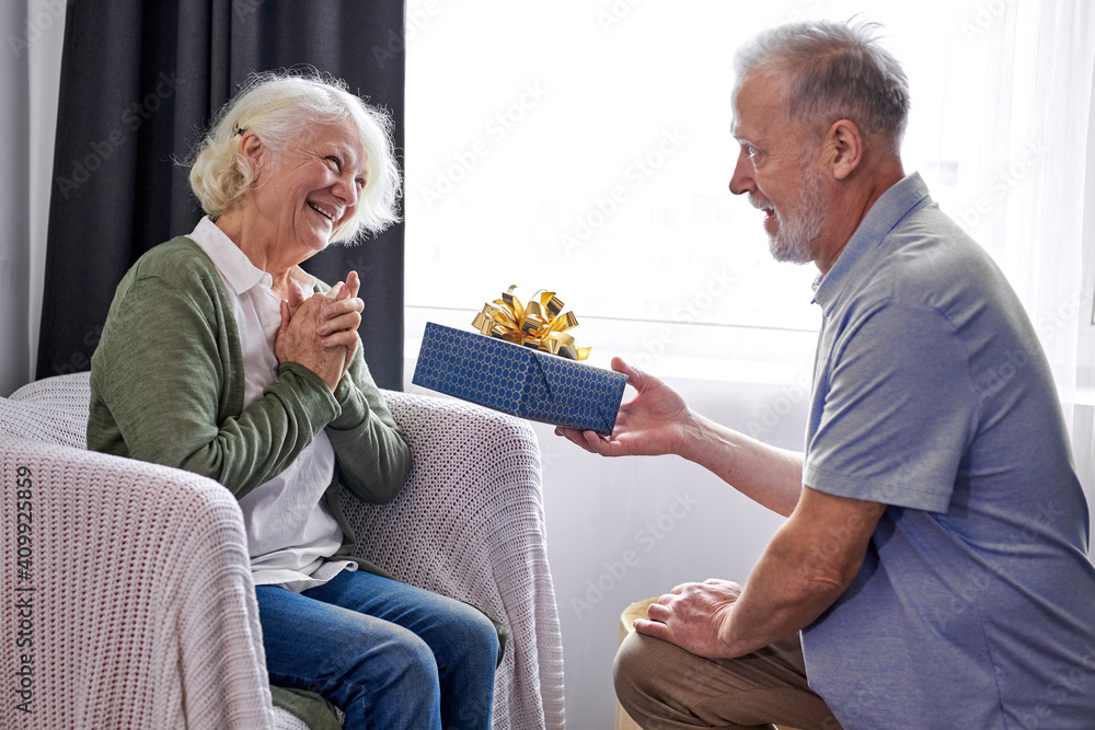 senior husband making surprise giving gift box to nice pretty wife, happy aged woman get unexpected present from spouse spending romantic weekend or celebrating anniversary together at home senior husband making surprise giving gift box to nice pretty wife, happy aged woman get unexpected present from spouse spending romantic weekend or celebrating anniversary together at home