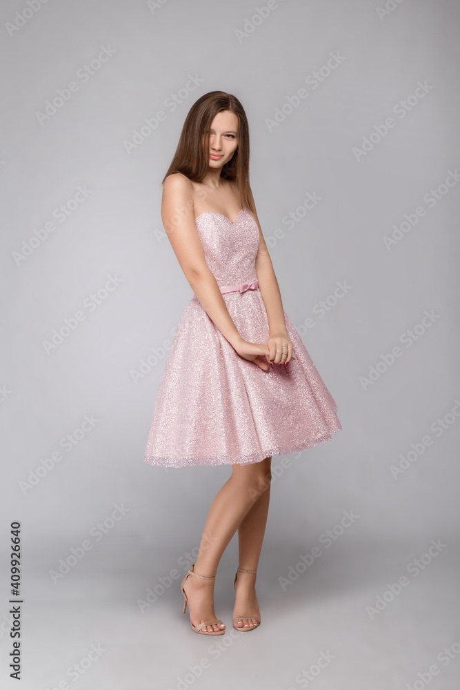Fototapeta premium Young beautiful girl in a pink dress stands on a gray background