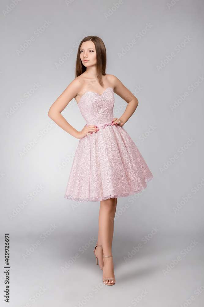 Young beautiful girl in a pink dress stands on a gray background Young beautiful girl in a pink dress stands on a gray background