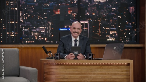 Canvastavla Late-night talk show host sitting behind his table and performing his monologue, looking into camera