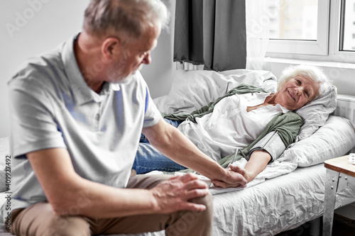 Obraz na plátně sick senior woman with her caring elderly husband sitting close to her, support and help