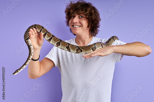 positive male holding snake in hands, doesn't afraid, no phobia. caucasian male in white t-shirt posing with snake