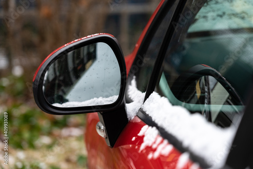 Rear-view mirror of a passenger car with powdery snow, close-up.