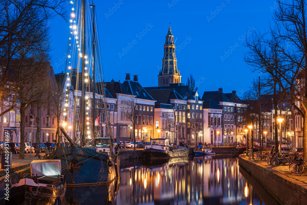 Old ships in a canal and the bell tower of the Aa-kerk in the historic city centre of Groningen.